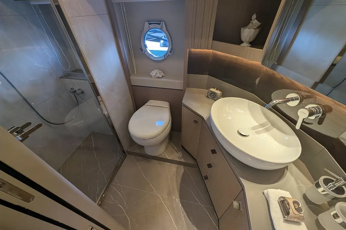 Modern bathroom featuring a shower, toilet, circular window, sink, and elegant wooden cabinetry with decorative items.